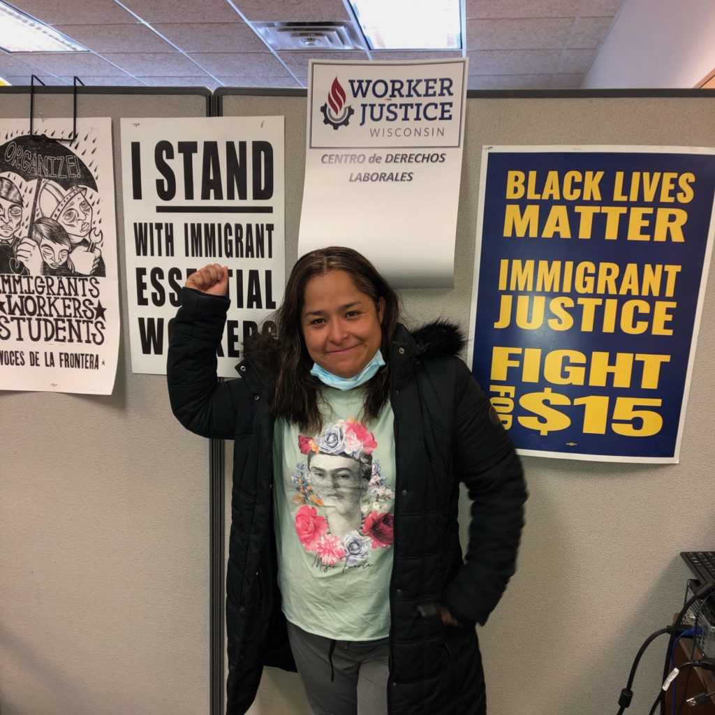 Worker Ruby Castaneda poses with her fist in the air in front of a Worker Justice Wisconsin sign.